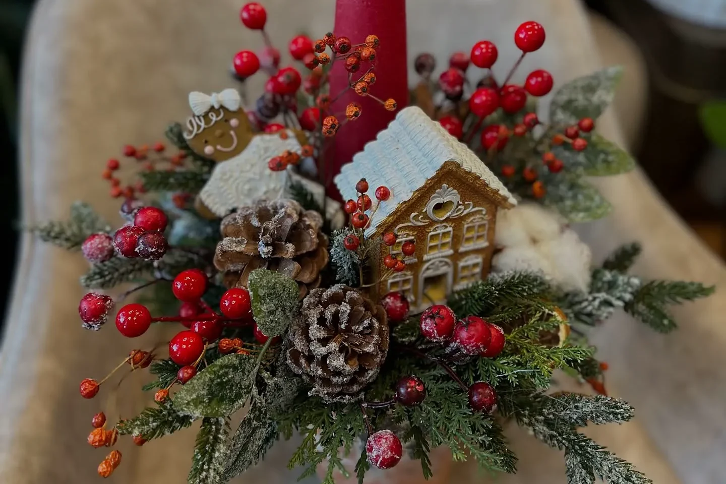 Świąteczny stroik z czerwoną świecą, gałązkami iglastymi i dekoracjami bożonarodzeniowymi